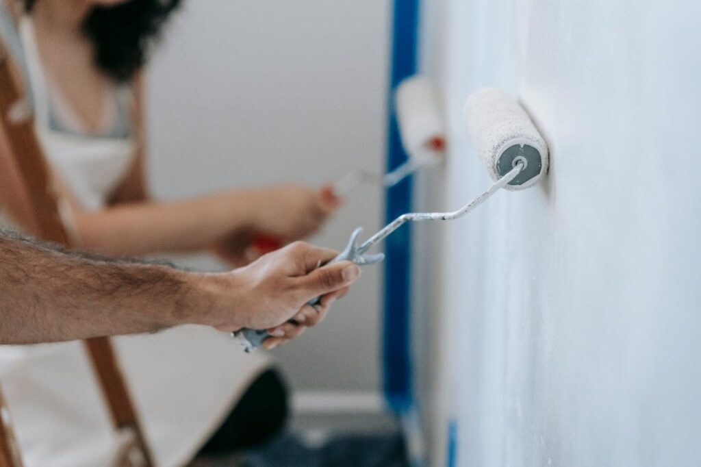 Couple painting a wall with rollers, perfect for home improvement and renovation themes.